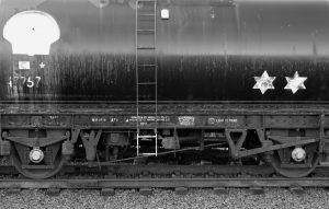 Vintage-style black and white photo of an oil tanker on railway tracks.