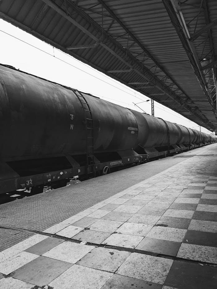 A grayscale image of a long cargo train at a railway station, showcasing industrial transport.