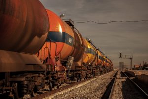 A long freight train with colorful tank cars on a railway track under a bright sky.